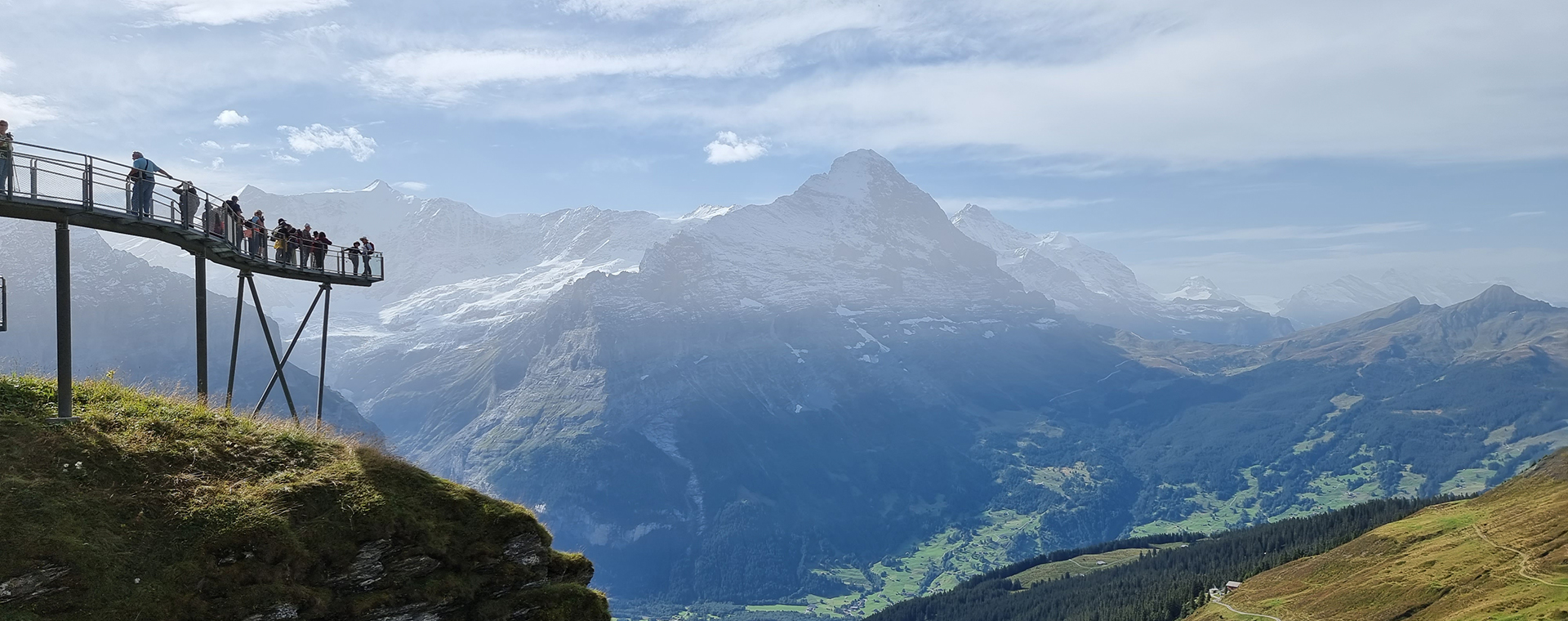Von einer modernen Plattform aus genießen Besucher den Panoramablick auf die majestätischen Schweizer Alpen bei Grindelwald. Die Aussicht umfasst schneebedeckte Gipfel und ein malerisches grünes Tal.