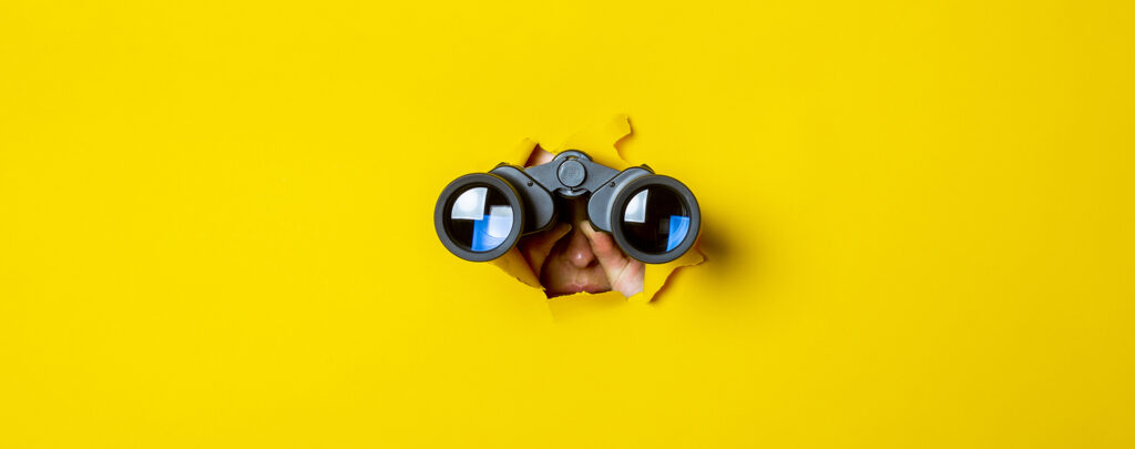 Neugieriger Blick in die Zukunft: Hände halten ein Fernglas durch ein gerissenes Loch in leuchtend gelbem Papier.