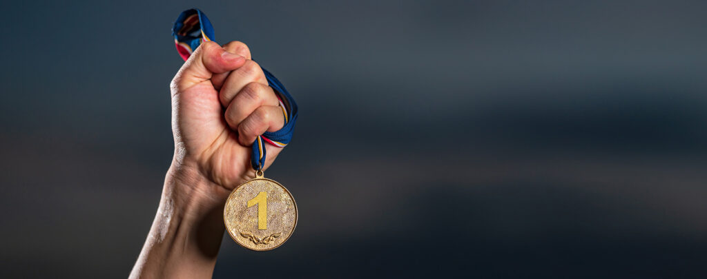 Hand mit goldener Medaille vor dunklem Hintergrund