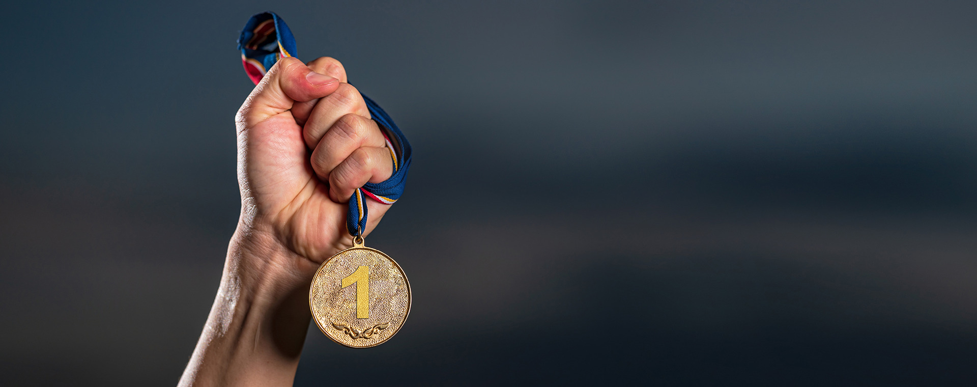 Hand mit goldener Medaille vor dunklem Hintergrund