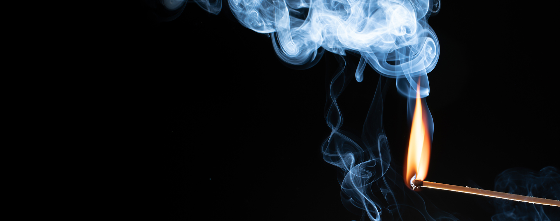 Ein brennendes Streichholz mit einer hellen Flamme und aufsteigendem blau-weißem Rauch vor einem tiefschwarzen Hintergrund.