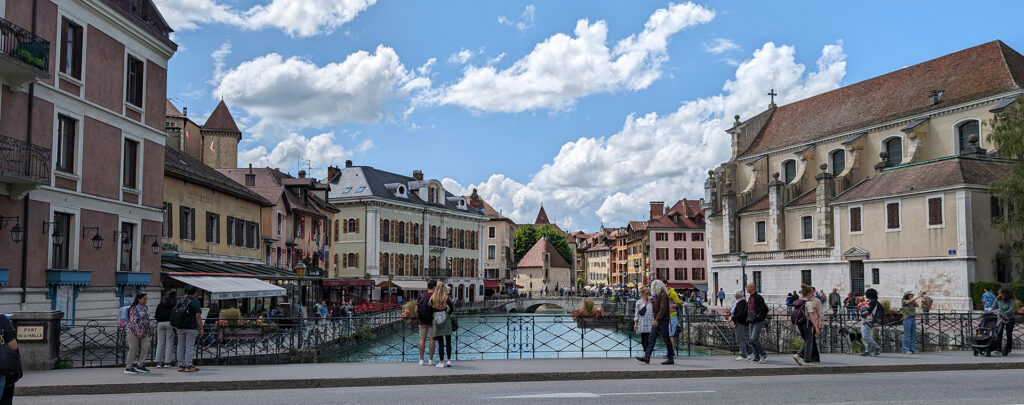 Blick auf einen malerischen Kanal in Annecy, Frankreich, umgeben von historischen Gebäuden und Menschen auf einer Brücke.